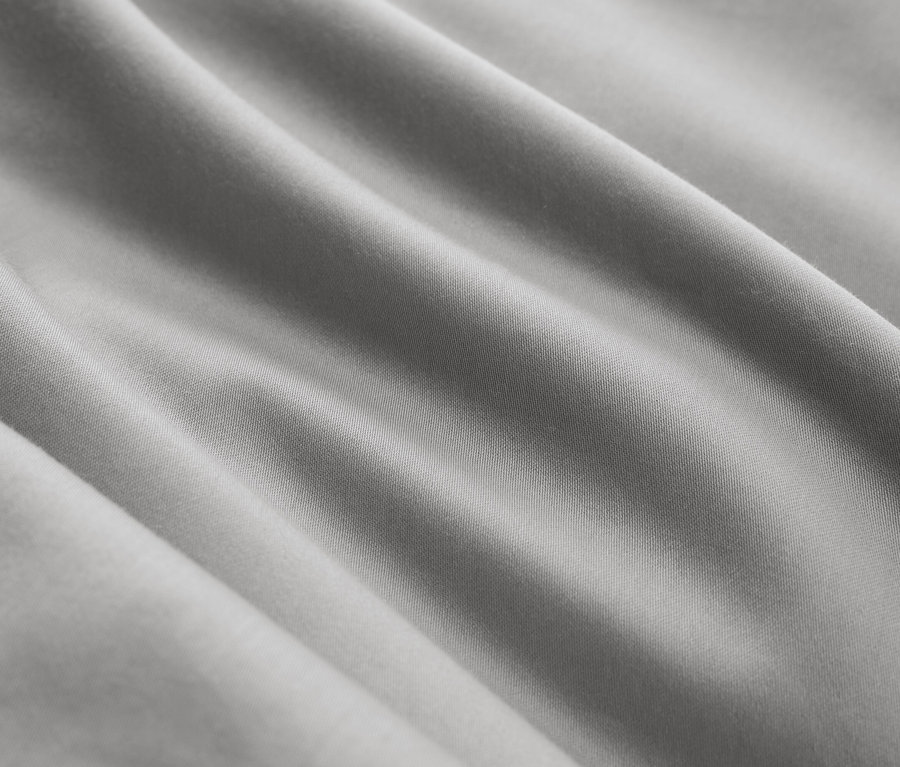 Detail šedej látky s diagonálnymi záhybmi.