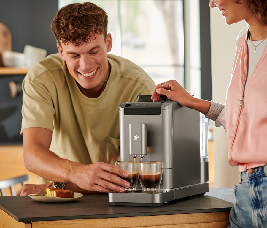 Muž sleduje, ako sa káva leje do dvoch pohárov z plnoautomatického kávovaru »Esperto2 Caffè« v Titanium Silver farbe.