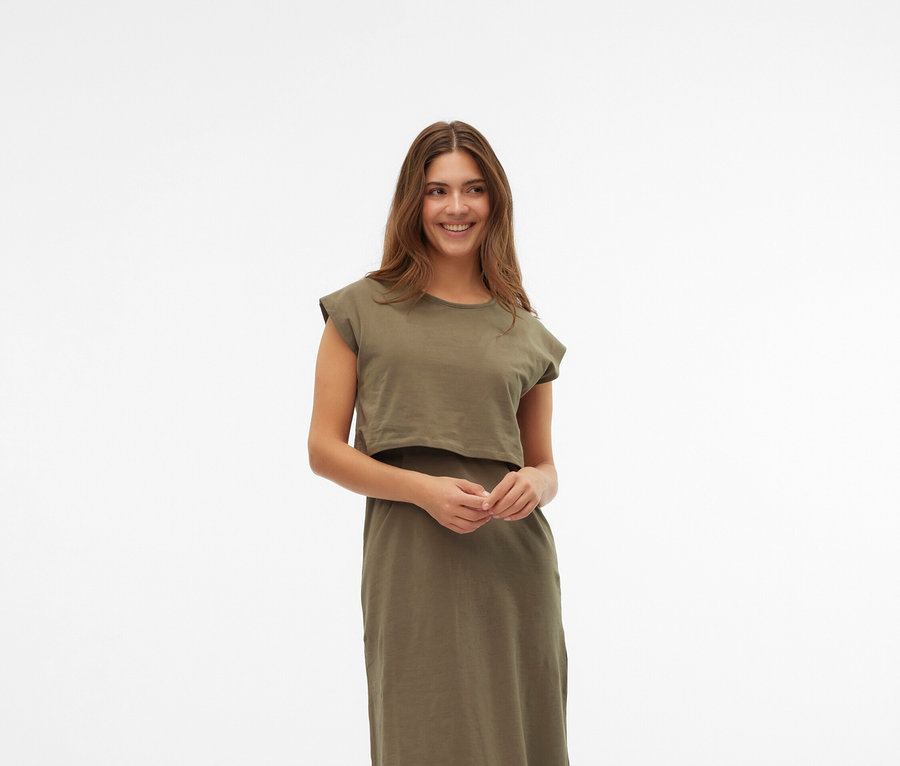 Žena má na sebe šaty khaki farby a krémové topánky Mary Jane na bielom pozadí.