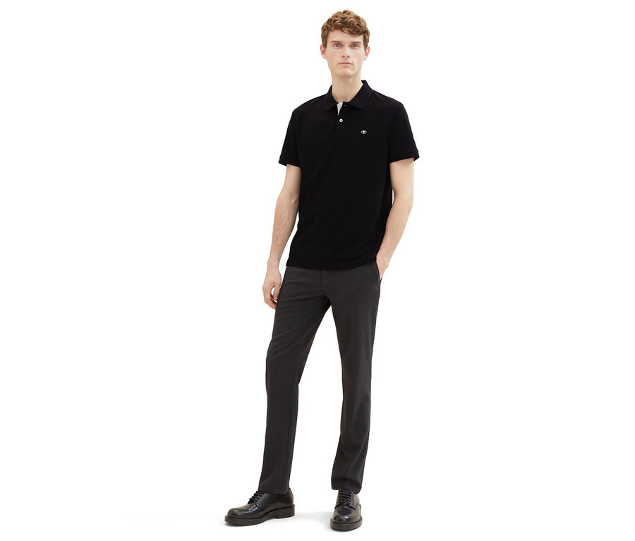 Muž v tmavých nohaviciach a čiernej piké polokošeli Tom Tailor.