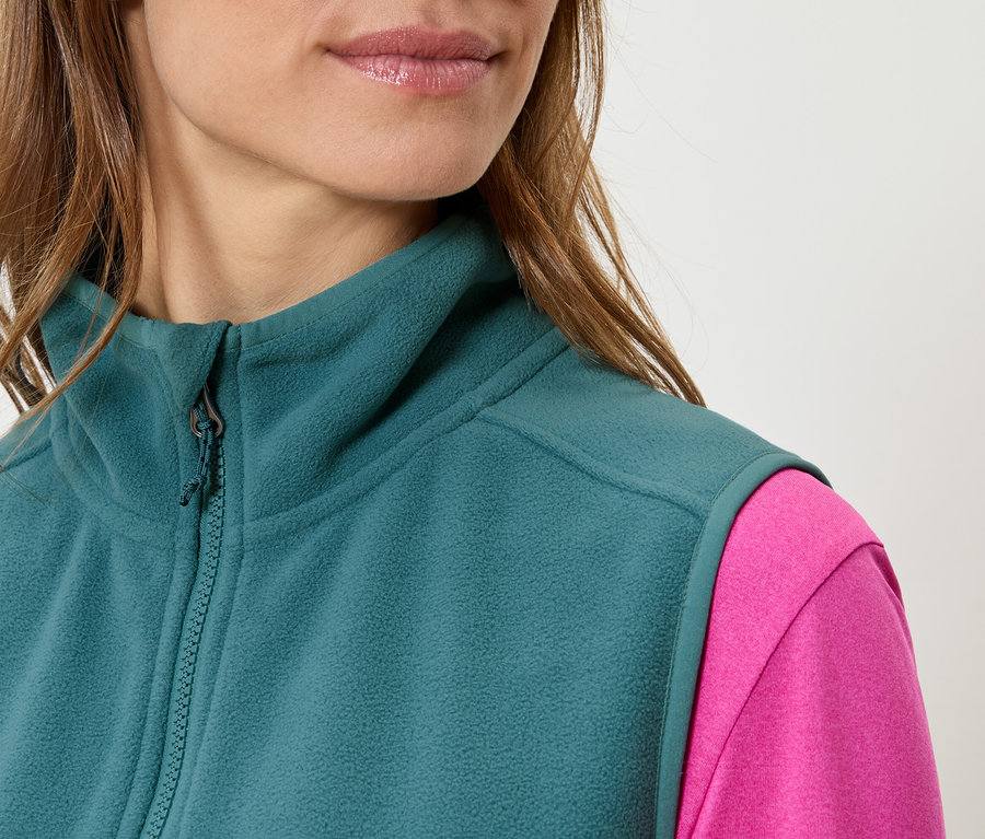 Detail ženy v petrolejovej flísovej veste cez ružový top.