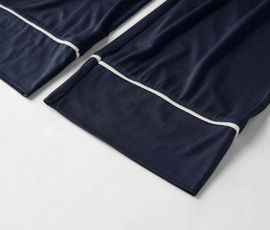 Detailný záber na tmavomodré pyžamové nohavice s bielym lemovaním na bielom pozadí.