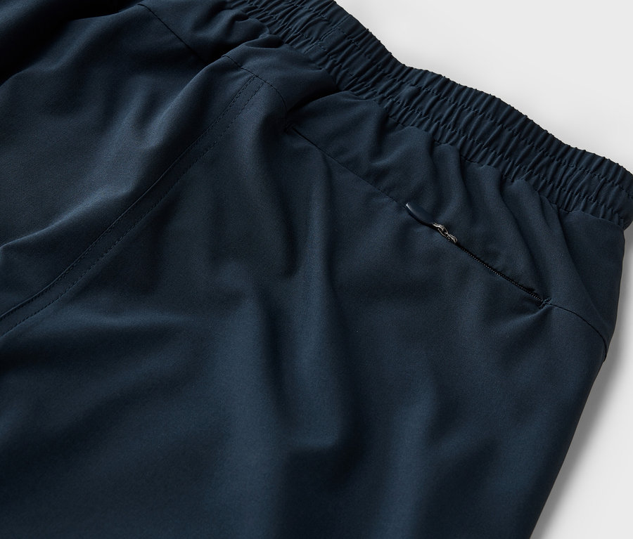 Detailný záber na tmavomodré tepláky s elastickým pásom a vreckom na zips na neutrálnom pozadí.