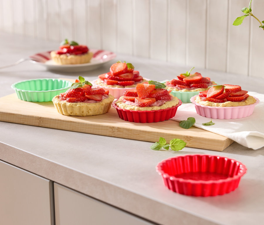 Niekoľko jahodových košíčkov vo farebných formičkách na drevenej doske, ozdobených mätou.