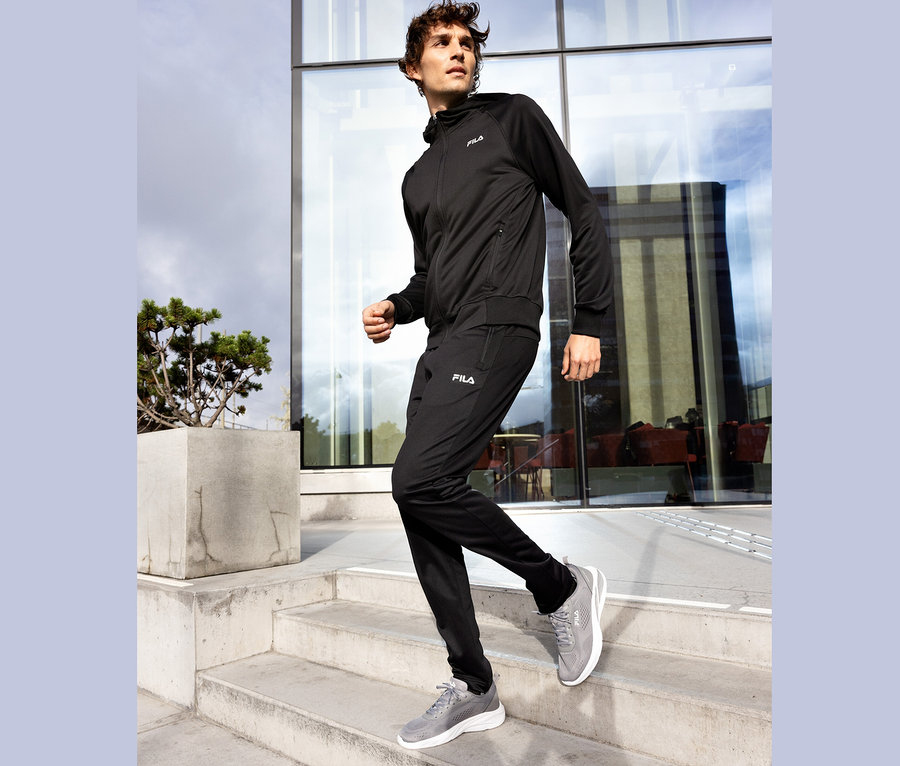Muž v čiernej teplákovej súprave Fila schádza po betónových schodoch, sivé topánky Fila.