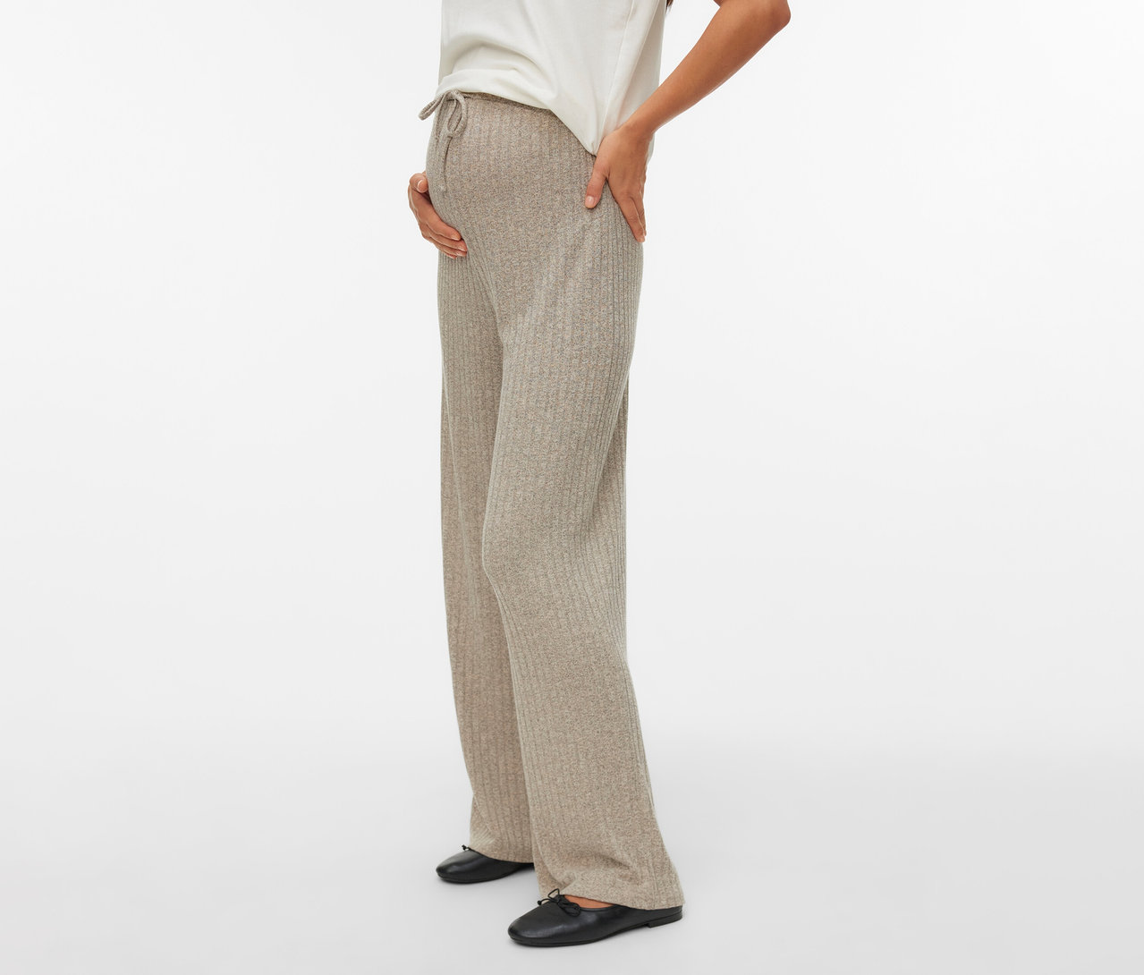 Tehotná žena s rukou na bruchu má na sebe nohavice MAMALICIOUS Loosefit »MLPAMMIE«, biele tričko a čierne topánky.