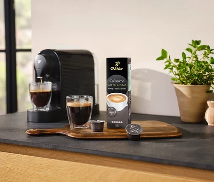 Kávovar pripravuje kávu do sklenice vedľa balenia Cafissimo Caffè Crema silná - 10 kapsúl.