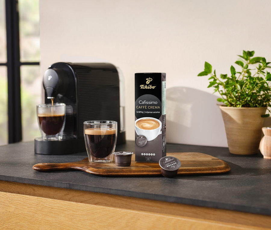Kávovar pripravuje kávu do sklenice vedľa balenia Cafissimo Caffè Crema silná - 10 kapsúl.