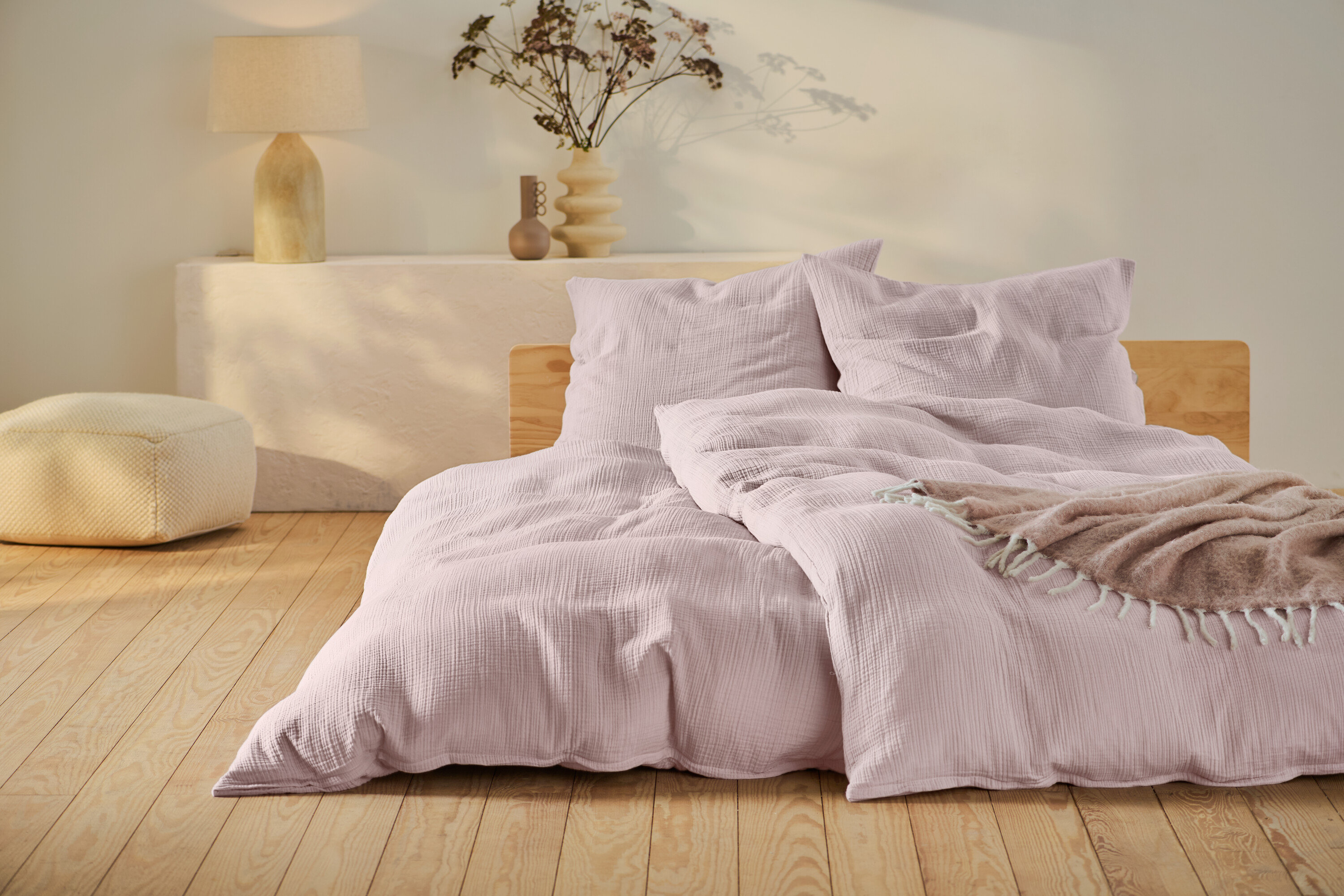 Ružové mušelínové obliečky štandardnej a nadmernej veľkosti na posteli s dreveným rámom.