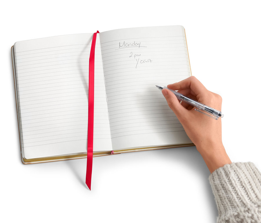 Ruka píše do poznámkového bloku s textilnou nášivkou.