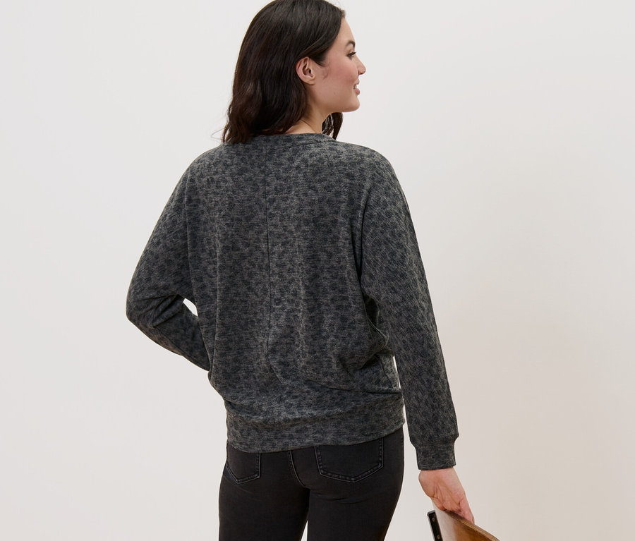 Žena stojí chrbtom a má na sebe tričko s netopierími rukávmi s potlačou a čierne džínsy.