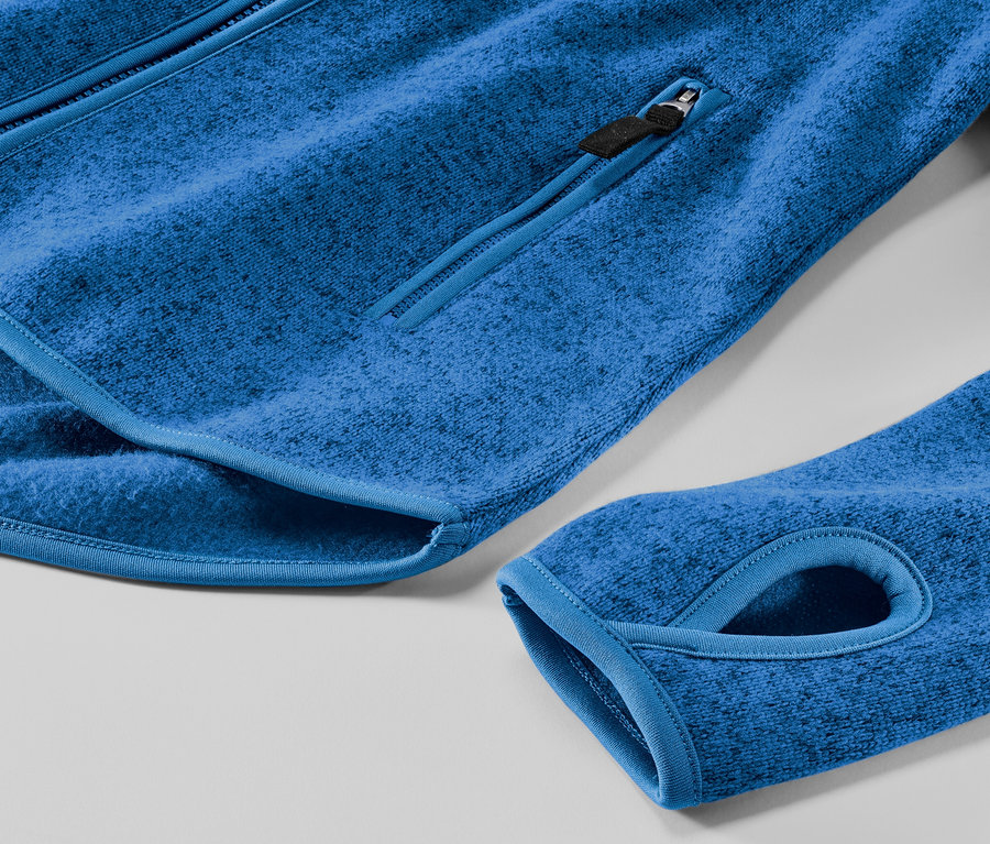 Detail modrej bundy z pleteného flaušu s vreckom na zips a otvorom na palec.
