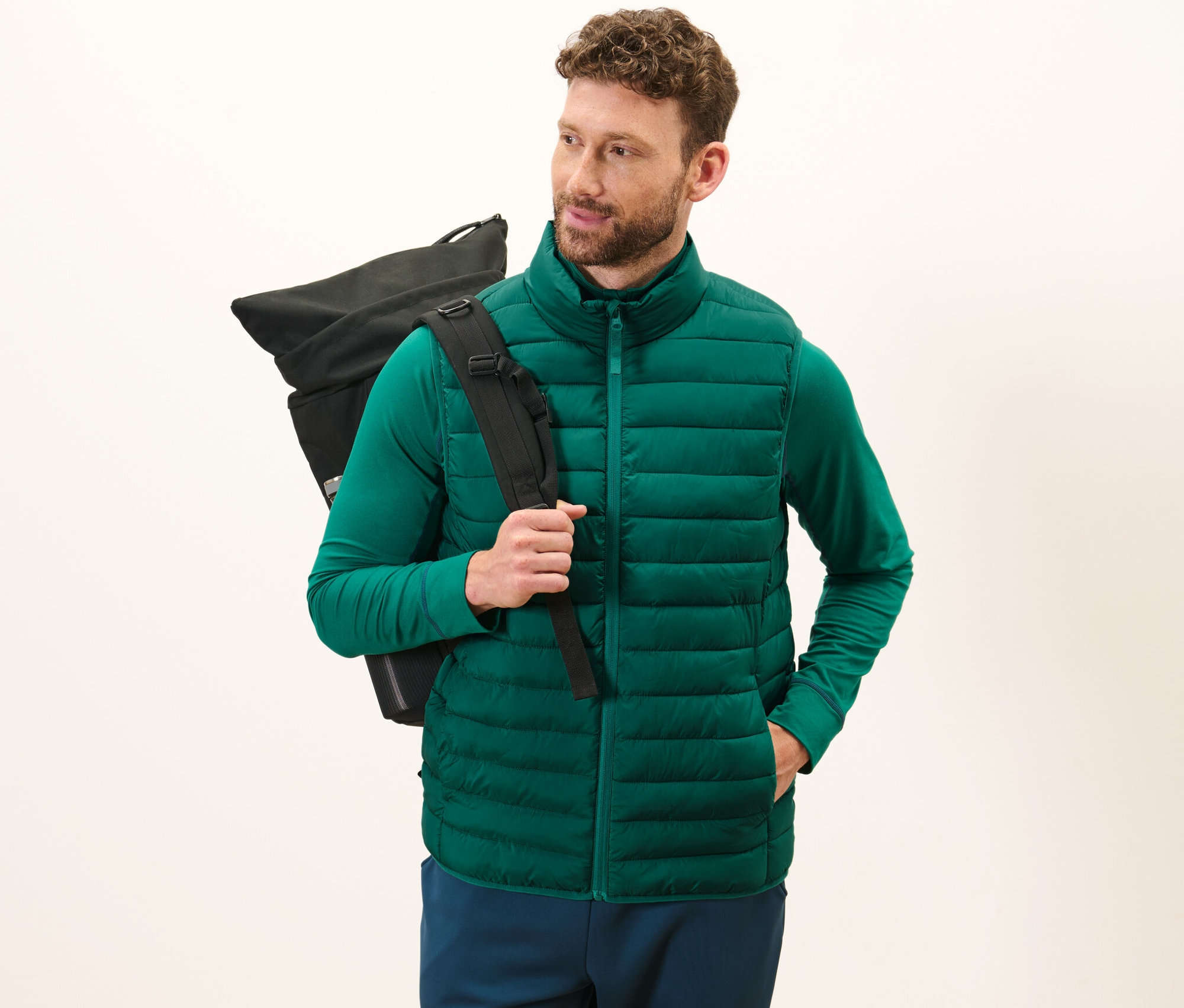 Muž má na sebe zelenú prešívanú vestu Skladacia prešívaná vesta a nesie čierny batoh.