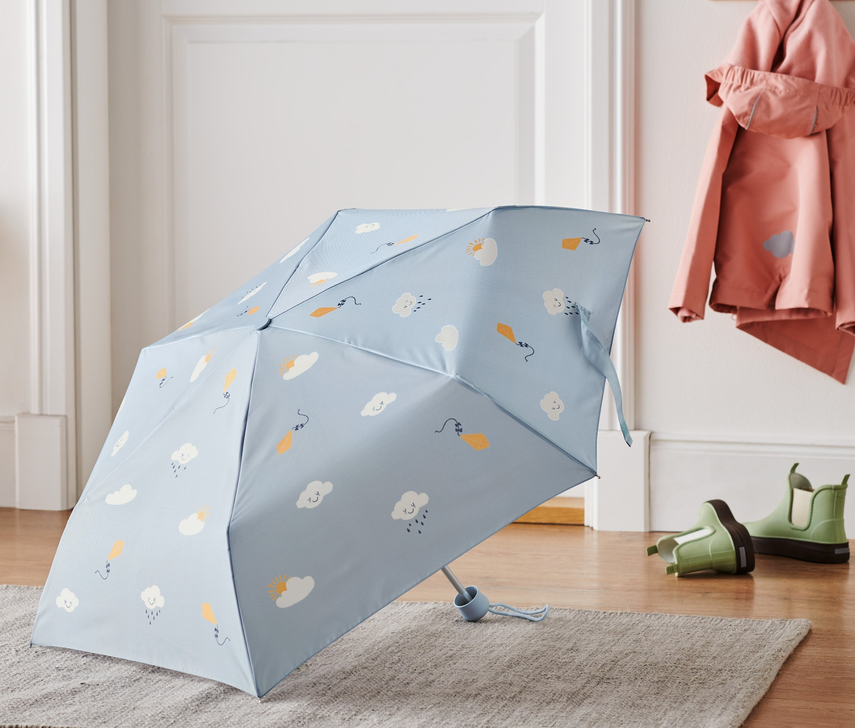 Svetlomodrý detský dáždnik s obláčikovým vzorom leží na sivom koberci.