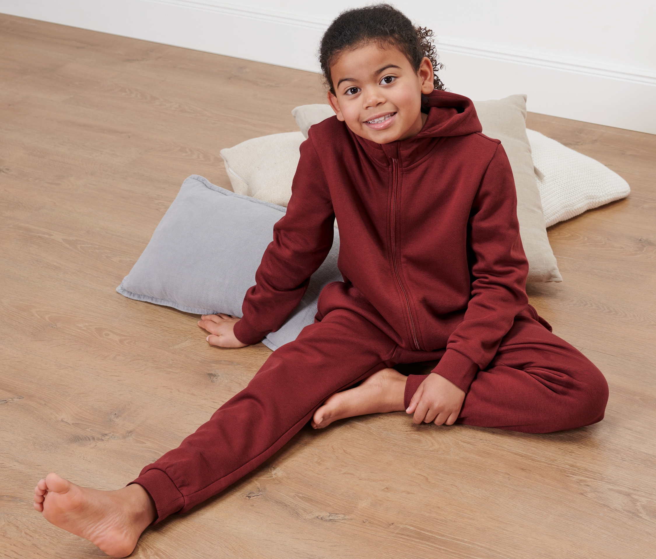 Dievča sedí na podlahe v červenom detskom pohodlnom overale.