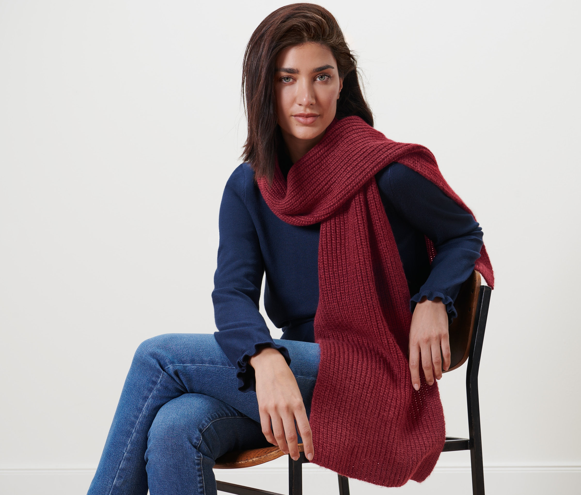 Žena sedí na stoličke a má na sebe pletený šál s vlnou.