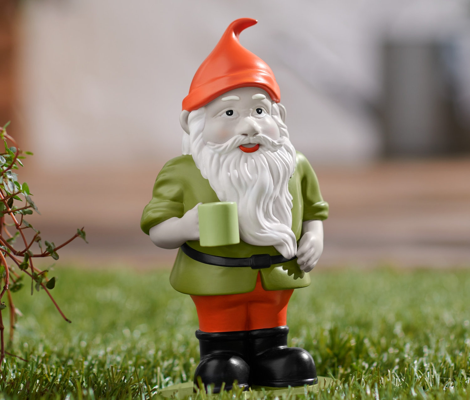 Záhradný trpaslík stojí na tráve a drží hrnček.