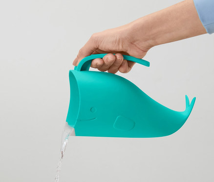 Ruka drží modrozelený detský pohár na kúpanie v tvare veľryby, z ktorého tečie voda.
