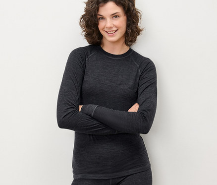 Žena pózuje so skríženými rukami v šedom funkčnom tričku s vlnou certifikovanou podľa RWS a nohaviciach.