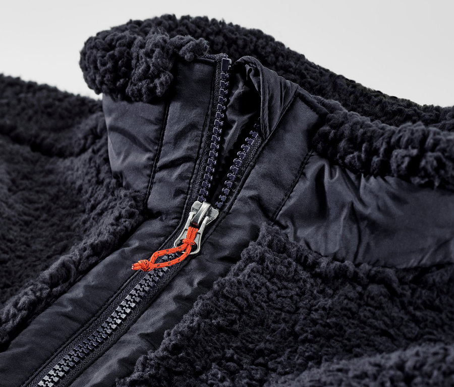 Detailný záber na plyšovú vestu s rozopnutým zipsom.
