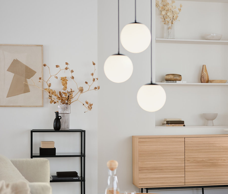 Obývacia izba s okrúhlym konferenčným stolíkom, odkladacou skrinkou »Finnsbo« s lamelovým vzhľadom a dizajnovým konzolovým regálom so sklenenými priehradkami. Nad nimi visí závesné svietidlo so sklenenými guľami.