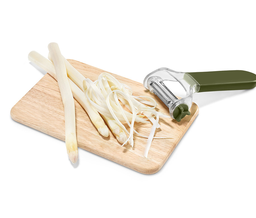 Na drevenej doske leží biely špargľa a univerzálna škrabka 3 v 1.