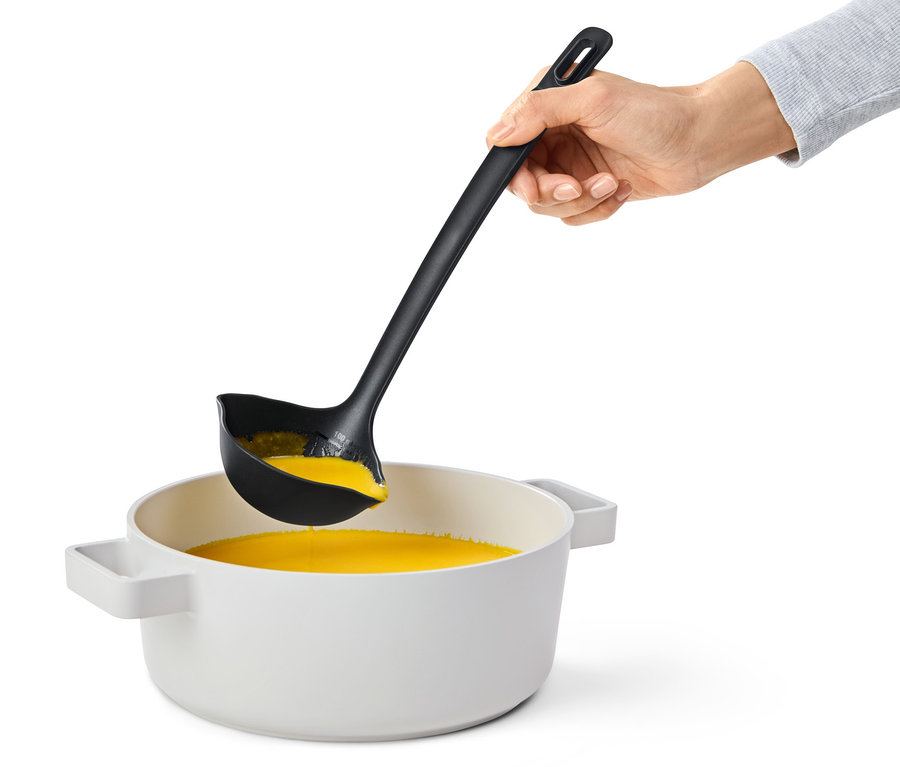 Ruka drží čiernu multifunkčnú naberačku nad hrncom s oranžovou tekutinou.