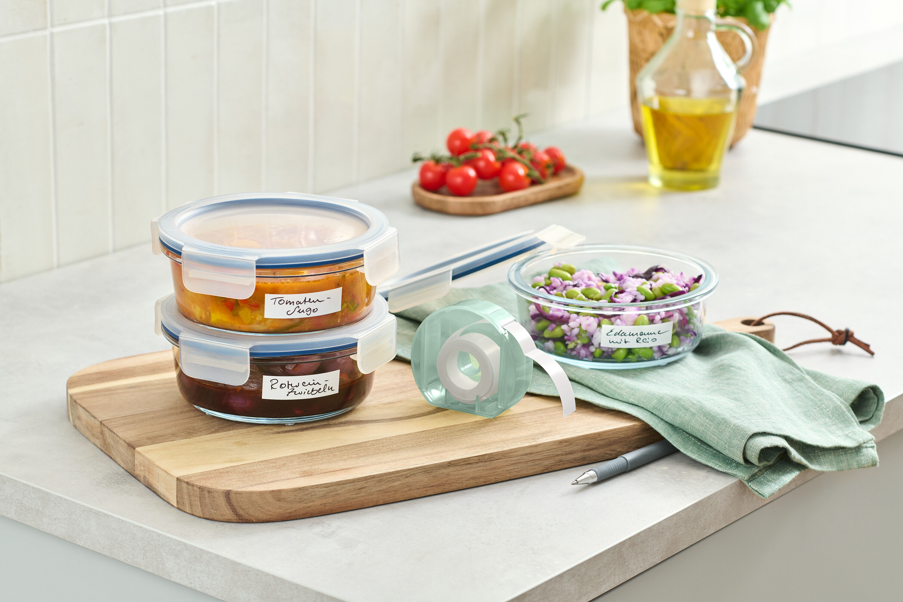 Dve sklenené nádoby s jedlom poukladané na drevenej doske vedľa rolky s etiketami.