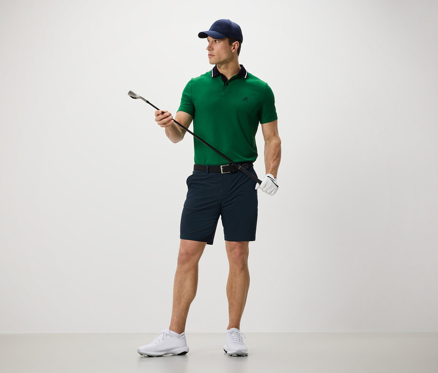 Muž drží golfovú palicu a má na sebe funkčné šortky.