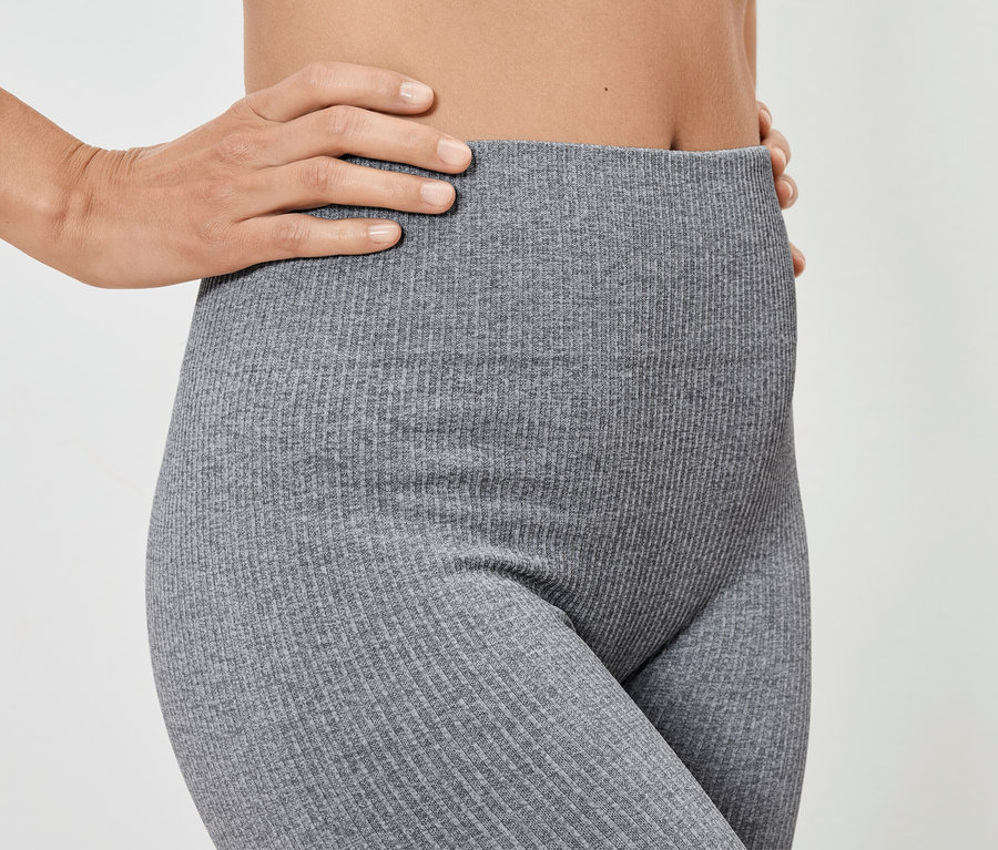 Žena pózuje v sivých rebrovaných legínach.