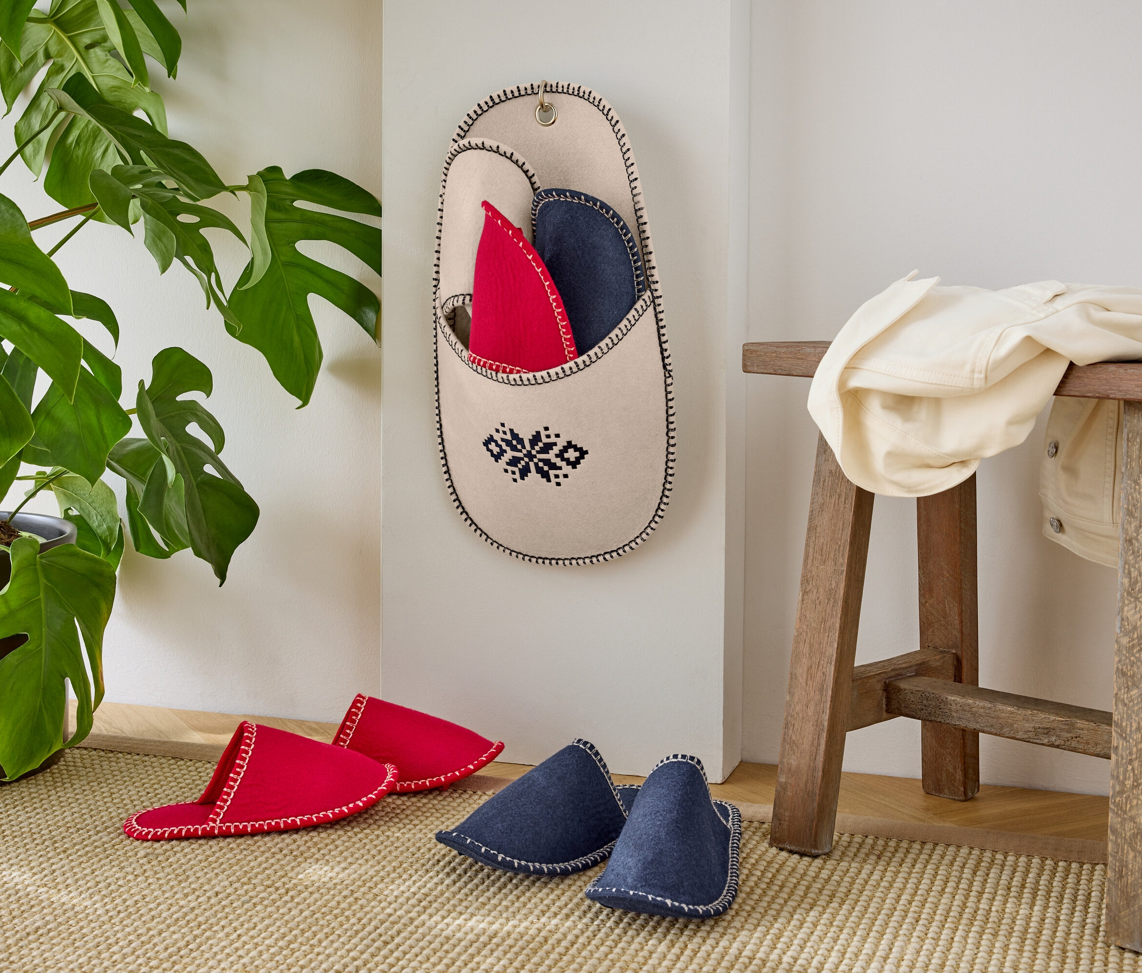 Červené a modré papuče pri stene s rastlinou v kvetináči.