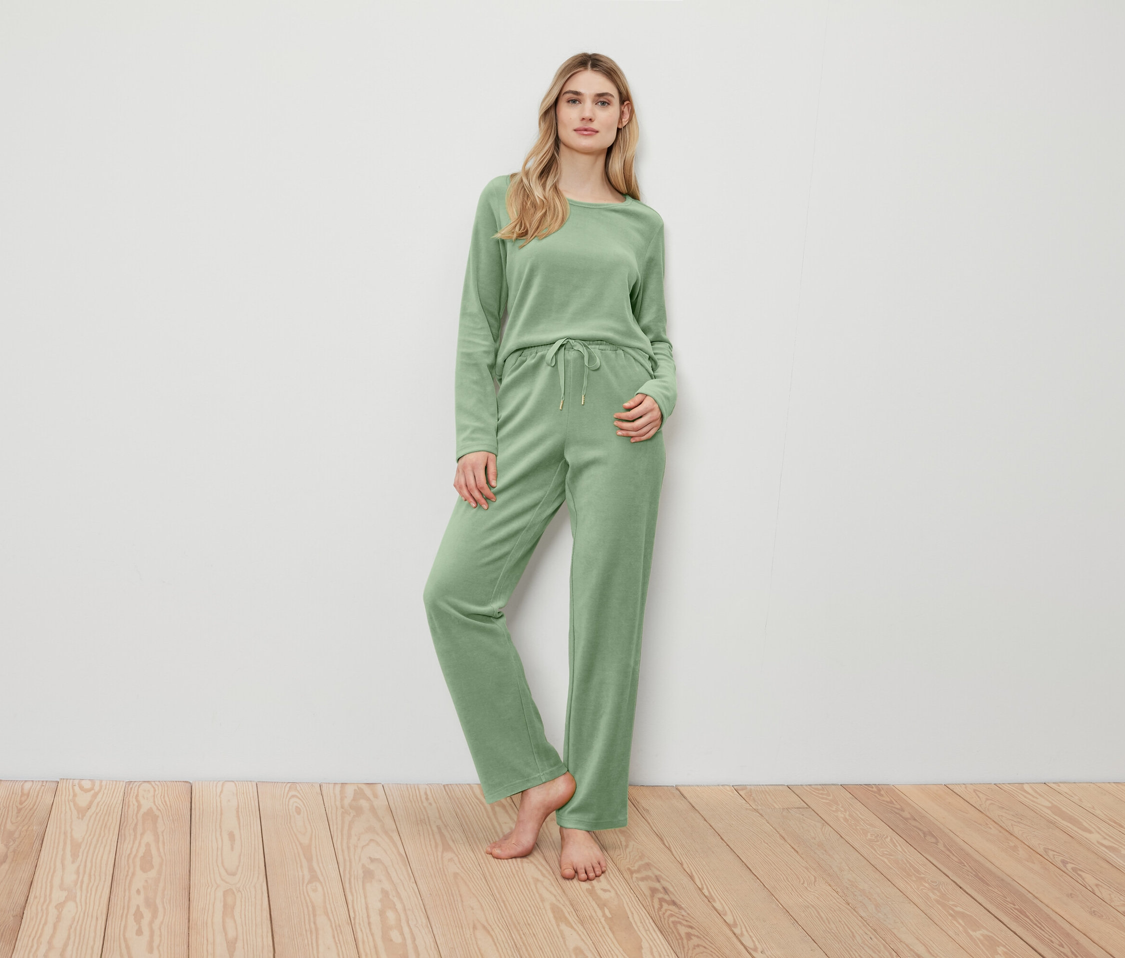 Žena pózuje v zelenom svetri a nohaviciach.