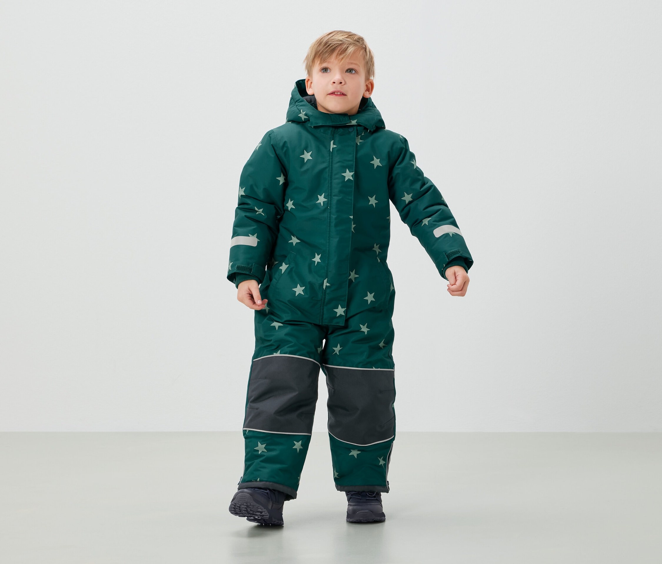 Chlapec stojí v zelenej kombinéze s hviezdami.