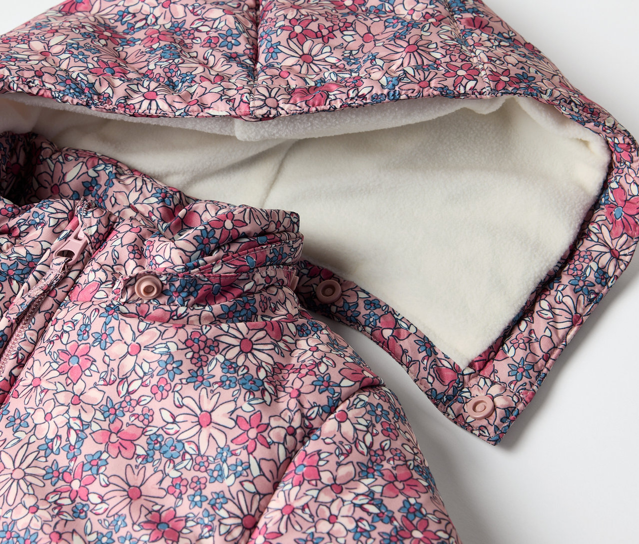 Detail zimného overalu pre bábätká s kvetinovým vzorom a kapucňou.