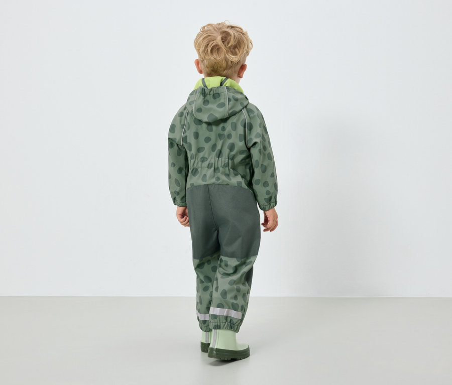 Chlapec v zelenom overale s kapucňou, chrbtom k fotoaparátu.