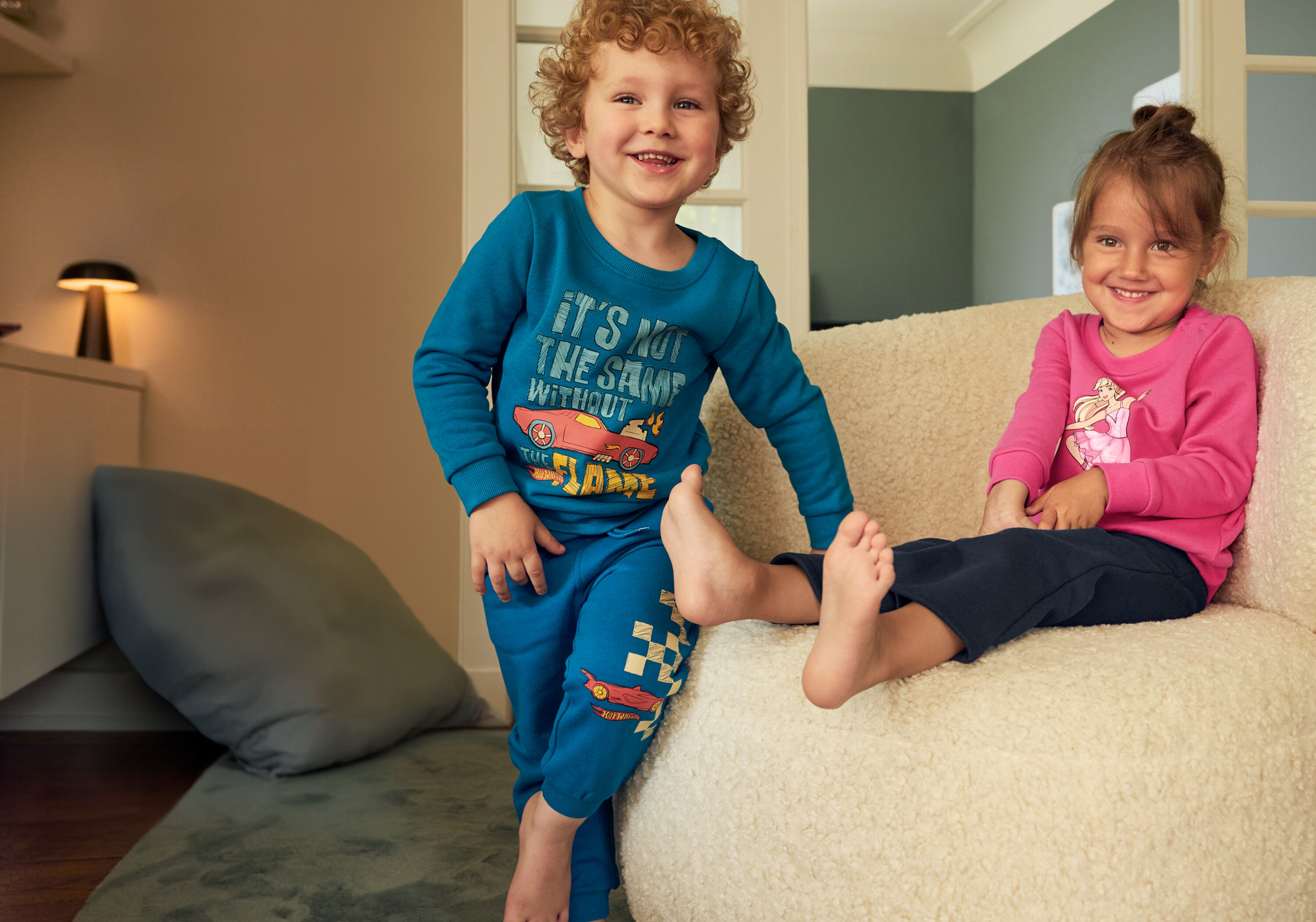 Chlapec v modrom komplete a dievča v ružovom sedia na béžovom kresle. Chlapec má na sebe 2 ks detských zvonových termo legínov s počesanou vnútornou stranou.