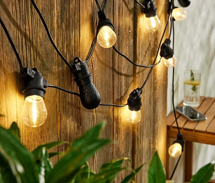 Svetelná LED reťaz s Bluetooth reproduktormi visí na drevenej stene. Na stole je pohár s nápojom a mobil.