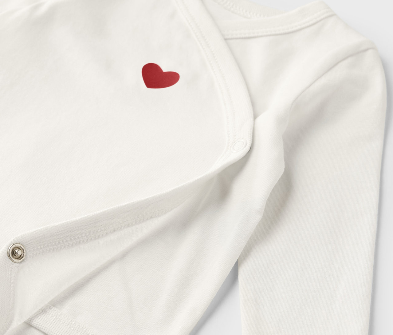 Detail bieleho rastúceho body pre bábätká s červeným srdiečkom.