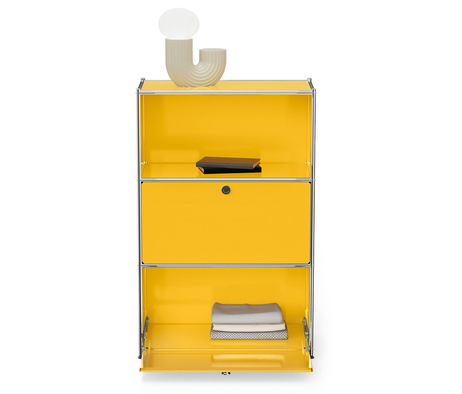 Žltá skrinka so strieborným rámom, hore lampa a kniha, dole zložené uteráky.