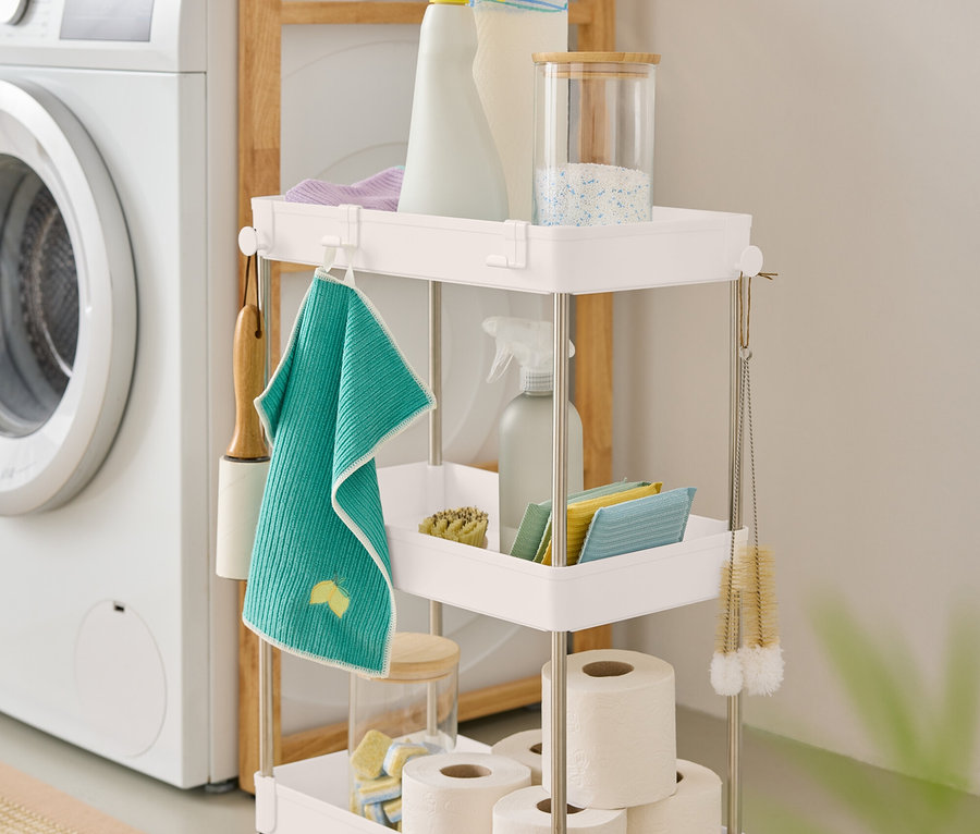 Trojposchodový biely vozík s čistiacimi prostriedkami stojí vedľa práčky.