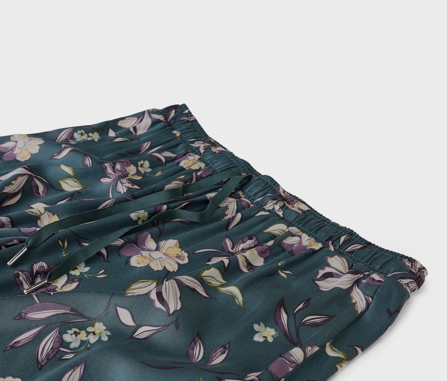 Detailný záber smaragdovozelených nohavíc s kvetinovou potlačou, elastickým pásom a šnúrkou.