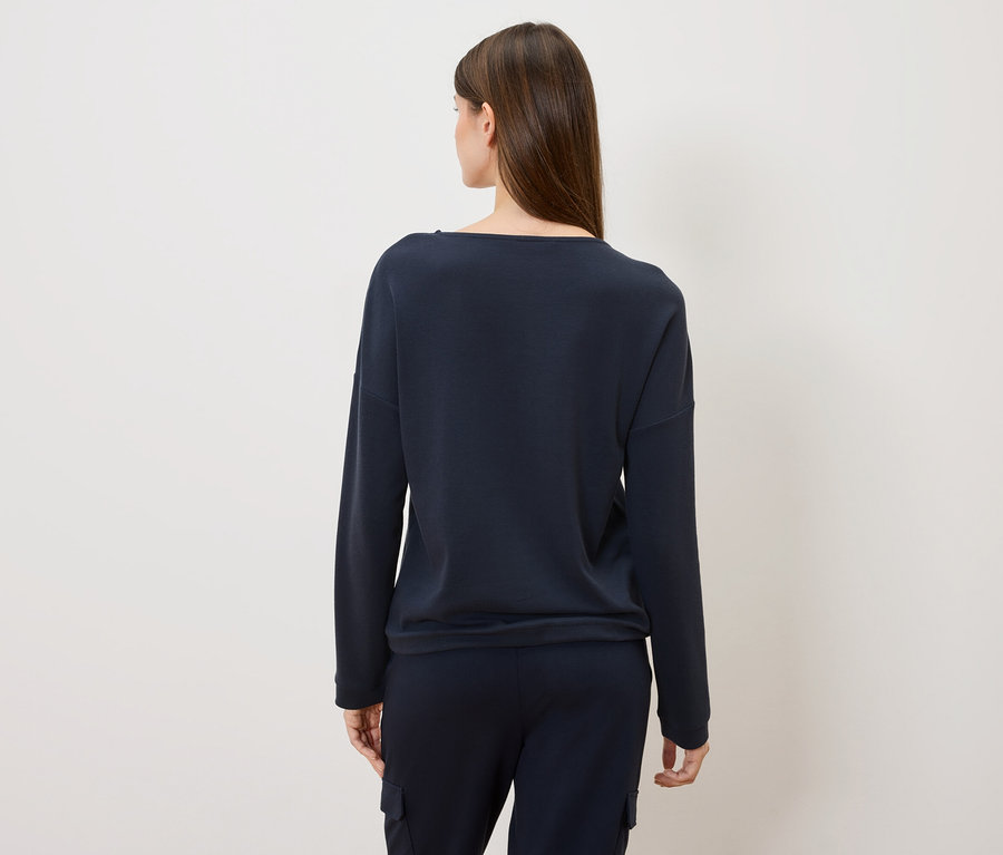 Pohľad zozadu na ženu s dlhými hnedými vlasmi v tmavomodrom svetri a nohaviciach.