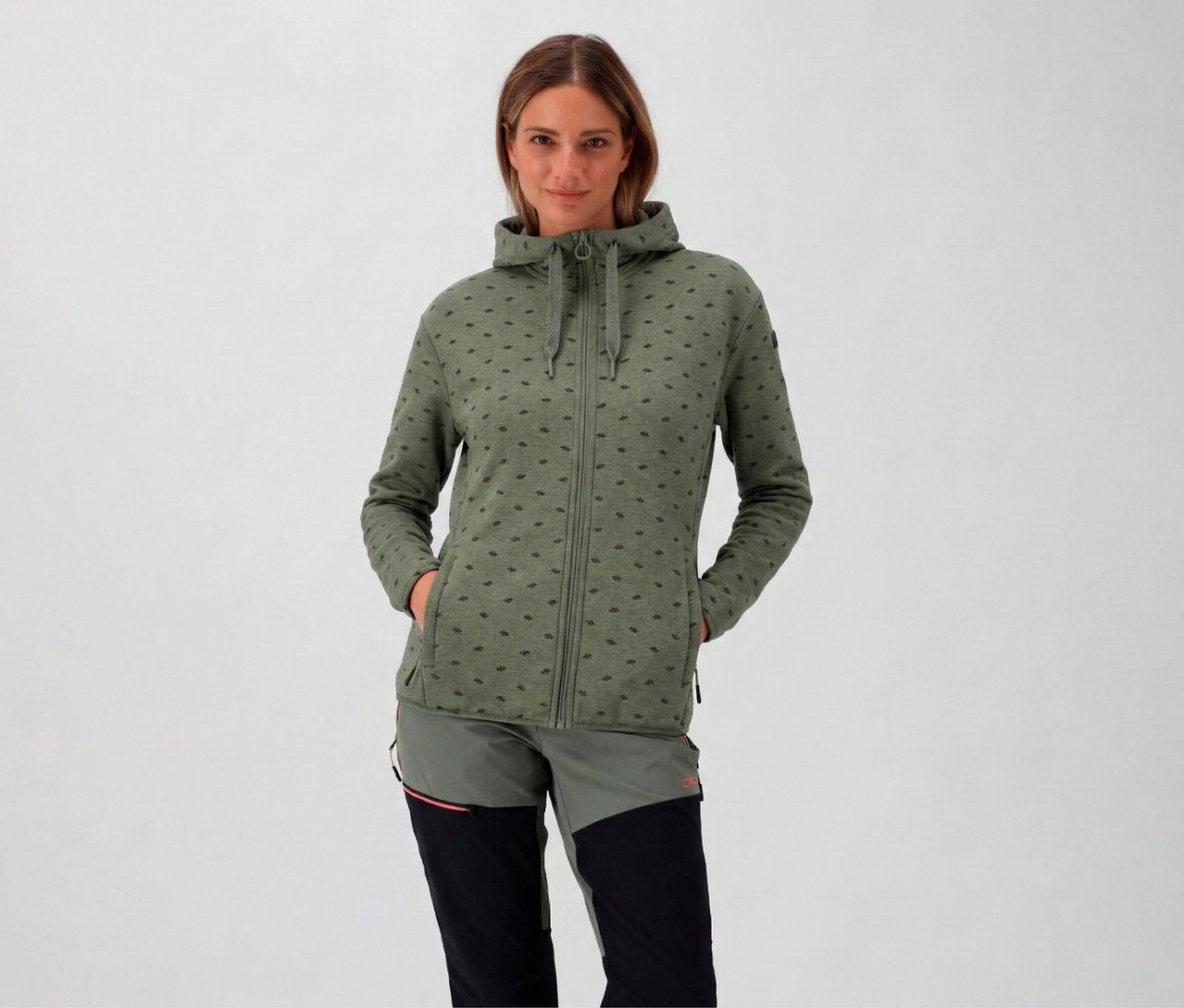 Žena s kapucňou má na sebe avokádovú dámsku flísovú bundu s kapucňou CMP a má ruky vo vreckách.