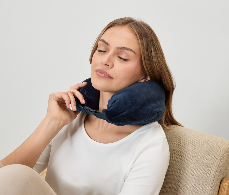 Žena so zatvorenými očami nosí tmavomodrú opierku krku, keď sedí v kresle.