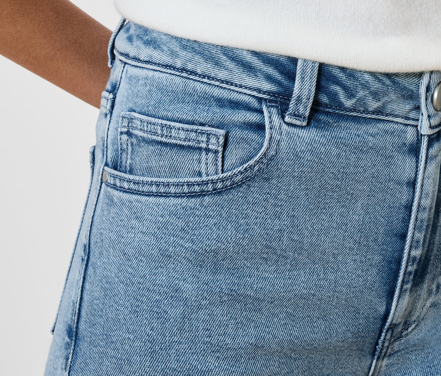 Detailný záber na svetlomodré rifle s vreckami a gombíkom.