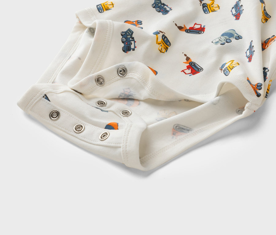 Detailný záber na biele detské body s potlačou stavebných vozidiel a patentkami.