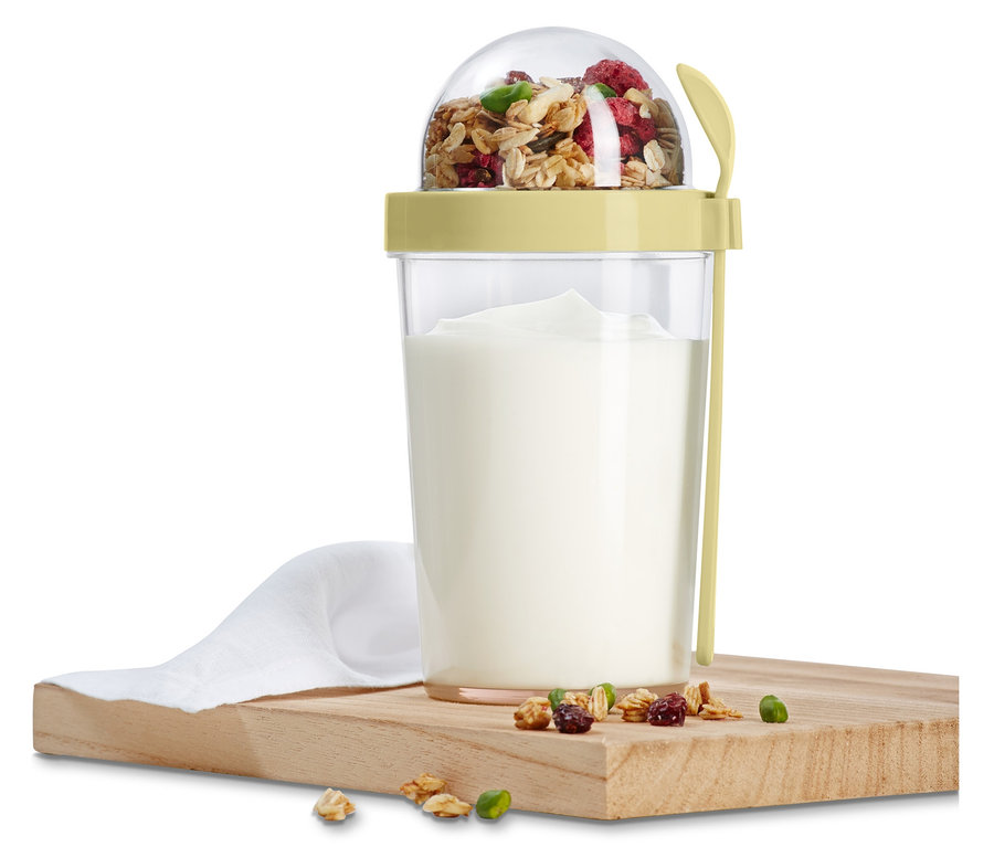 Cestovný box na jogurt s müsli a lyžičkou stojí na drevenej doske.