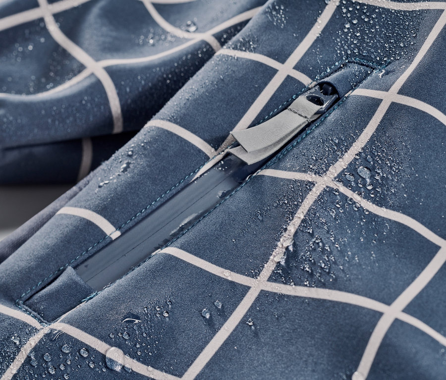 Detail detského softshellového overalu s kockovaným vzorom so zipsom a kvapkami vody.