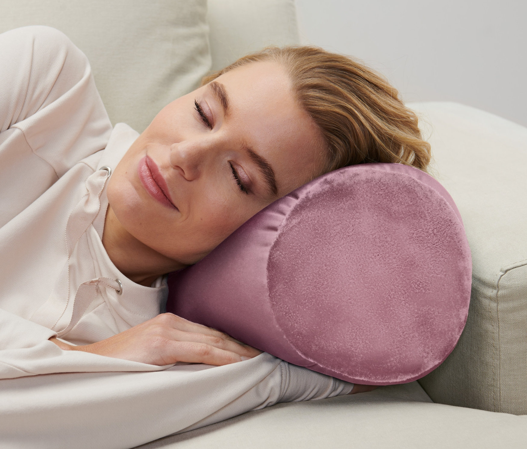 Žena spí na béžovej pohovke s relaxačným vankúšom.