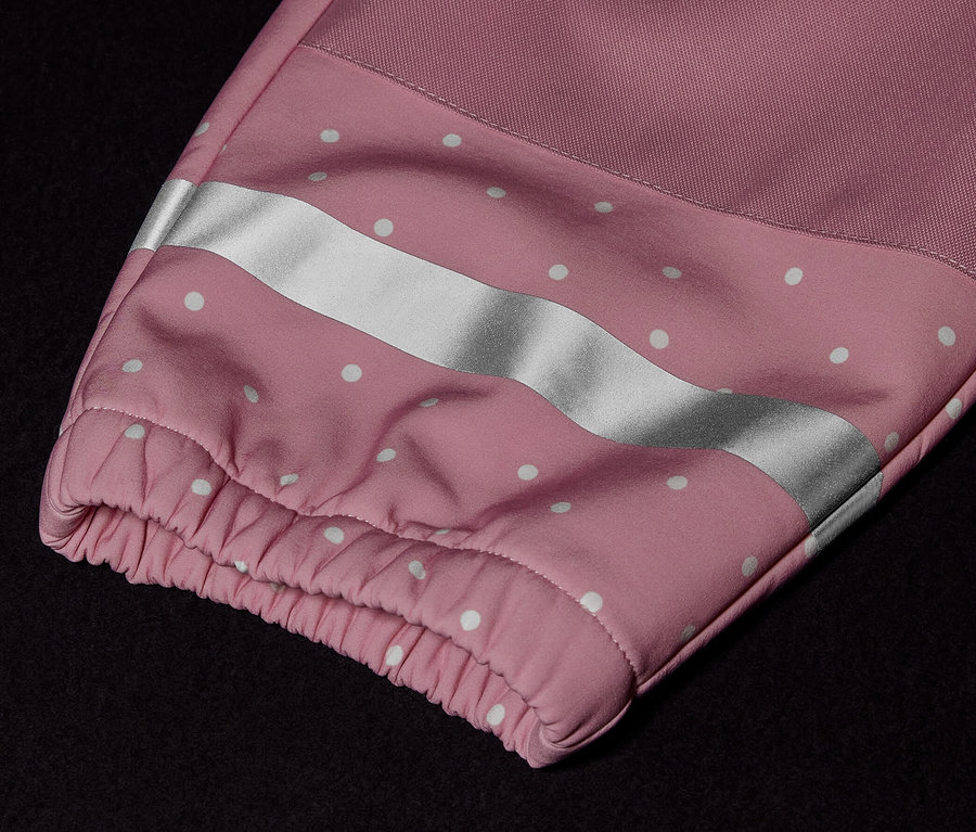 Detail detskej softshellovej kombinézy s ružovým rukávom, bielymi bodkami a reflexným pruhom.